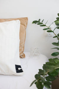 Funda de almohada de conexión a tierra Earthle sobre una almohada en una cama hecha, con una planta al lado