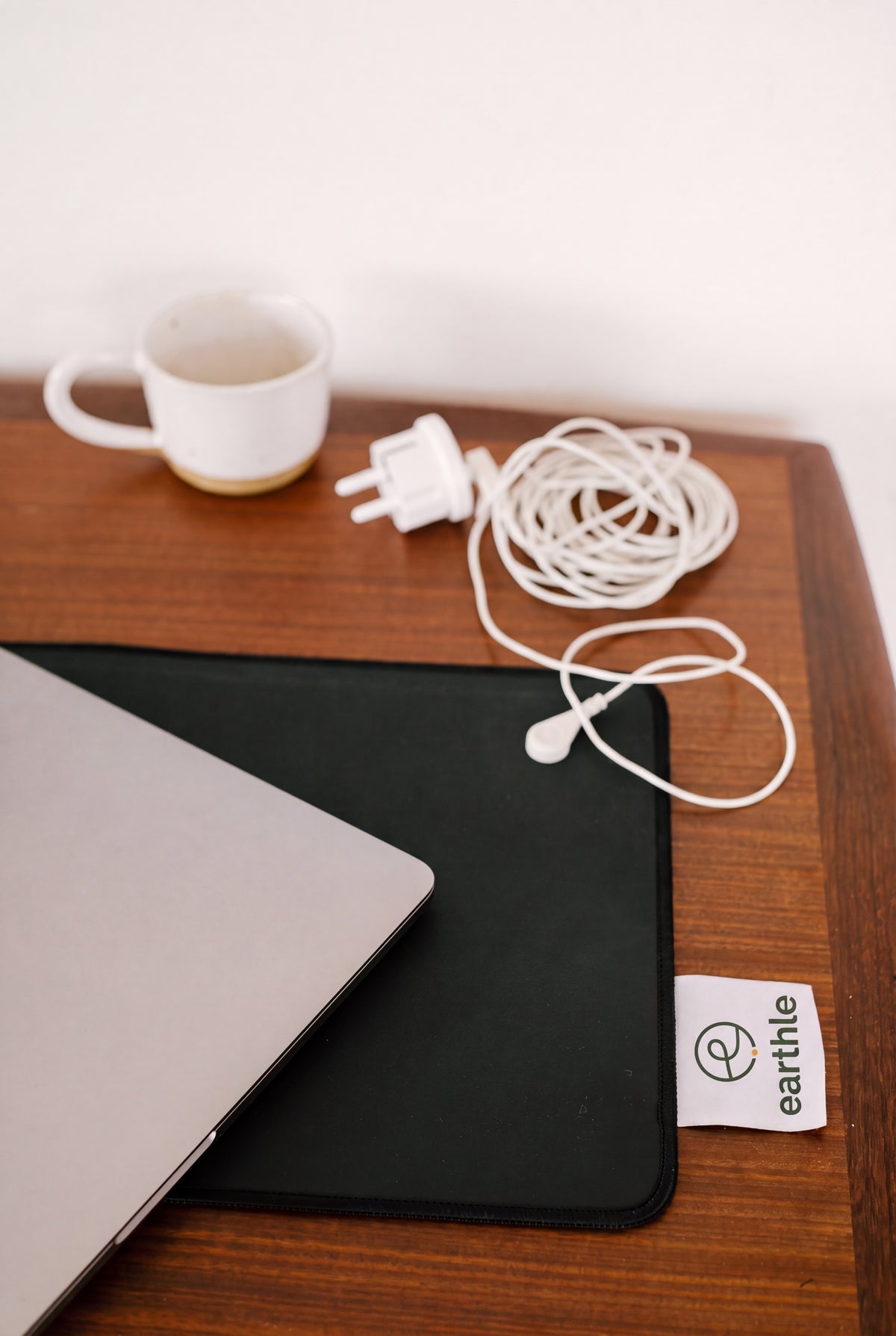 Alfombrilla de escritorio de conexión a tierra Earthle sobre un escritorio de madera con portátil, taza de café y el cable enrollado