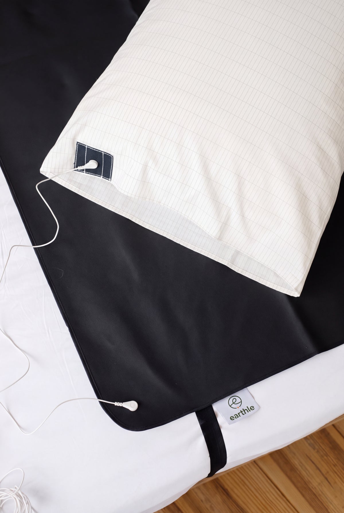 Funda de almohada de conexión a tierra Earthle sobre una cama junto a la esterilla de conexión a tierra negra, con el cable de conexión a tierra